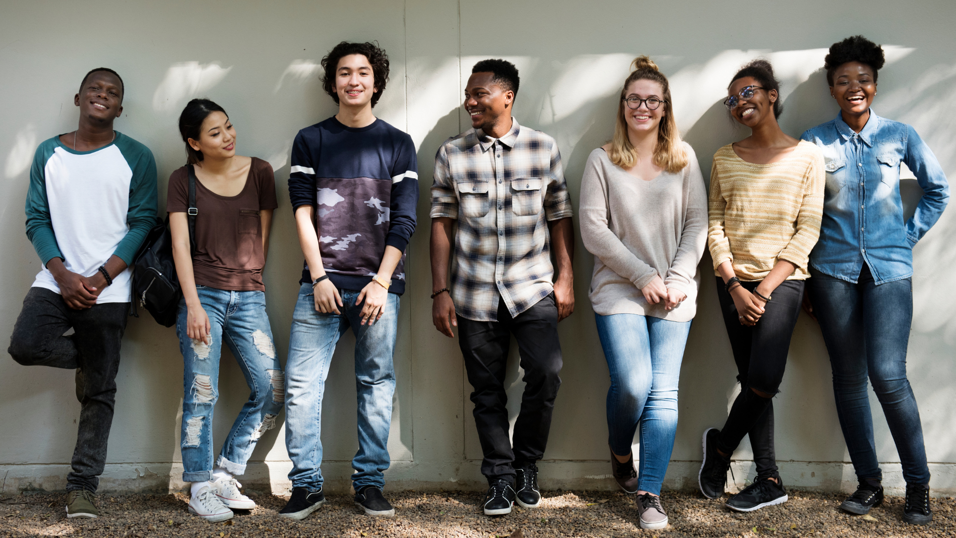 Teens standing smiling against sunny wall outside